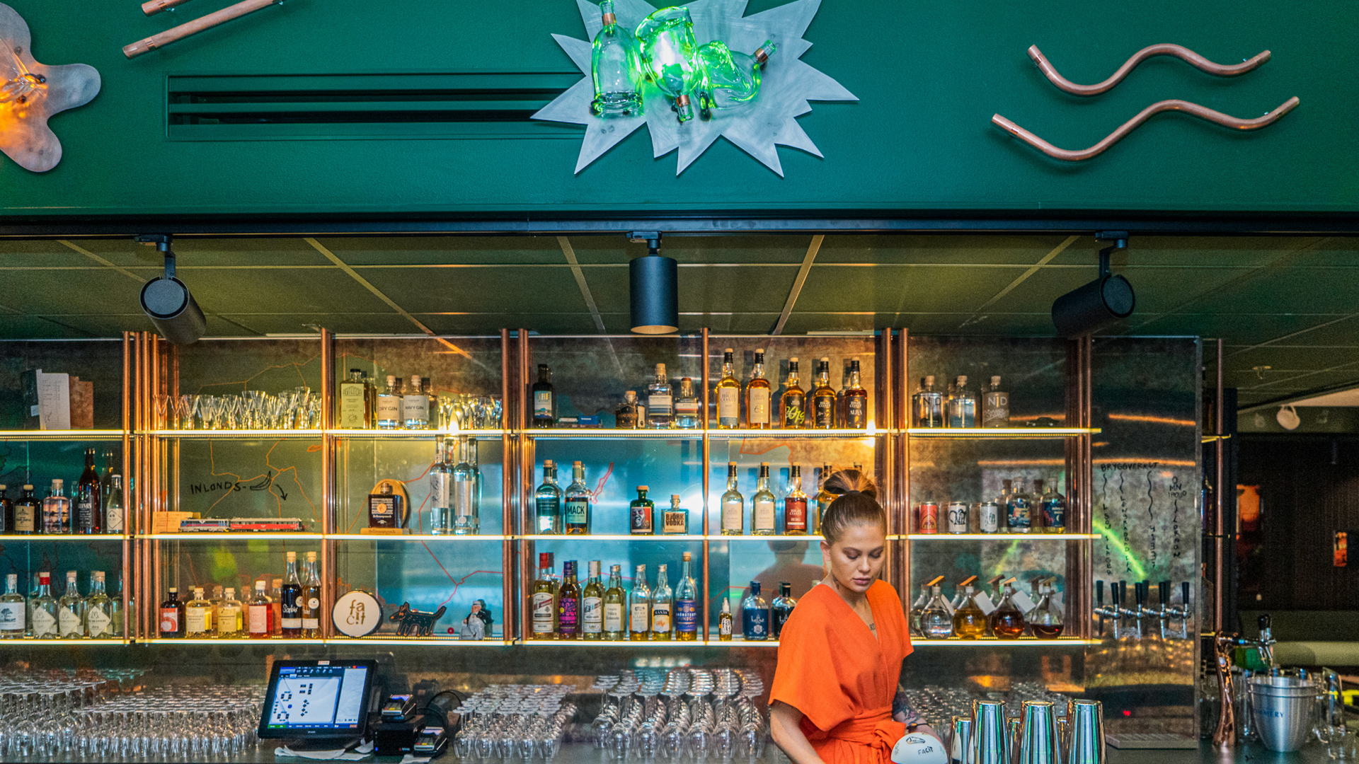 A woman in an orange dress is standing in a green bar. 