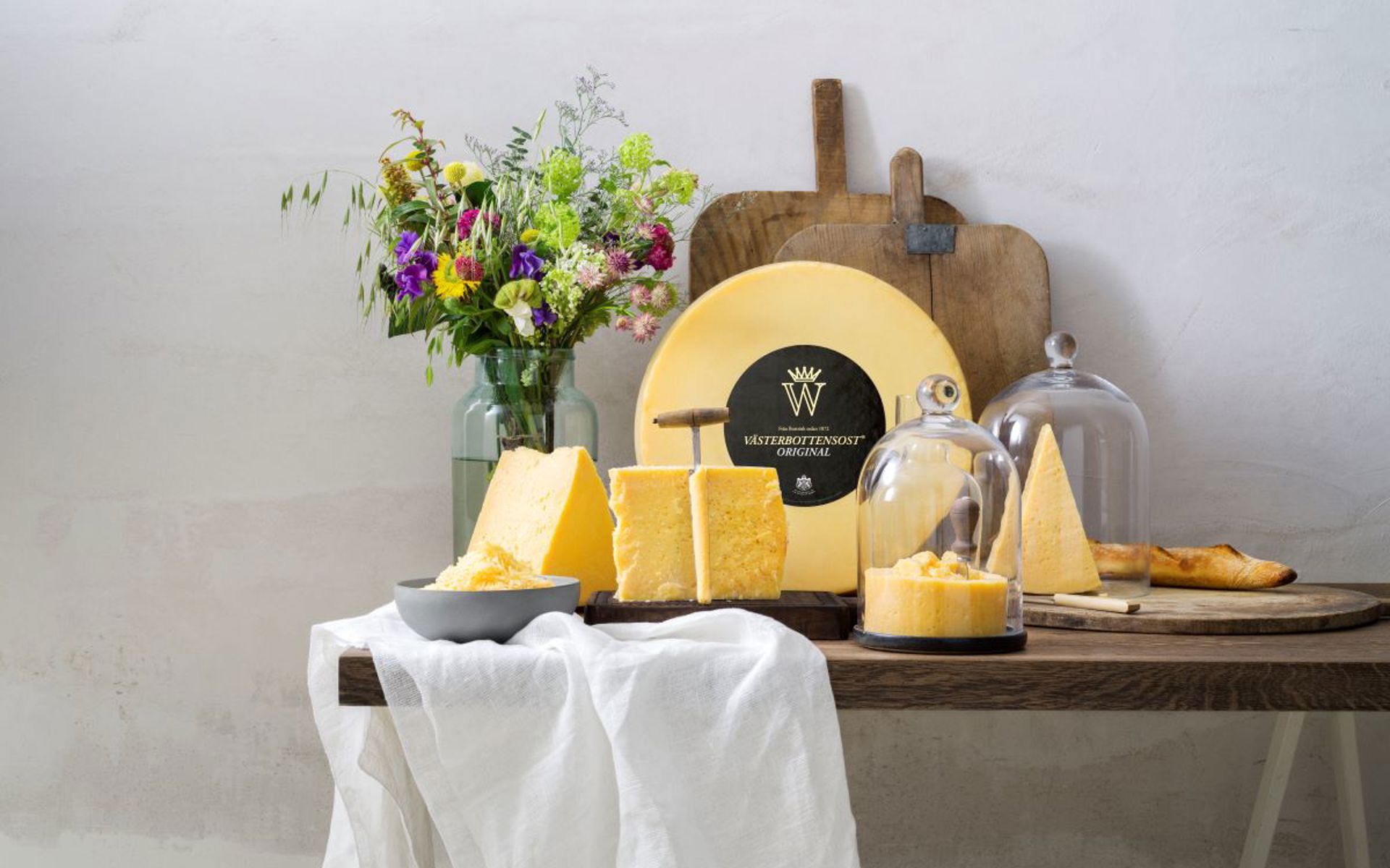 Cheese on a rustique table, with a bouqet of flowers to the left. 